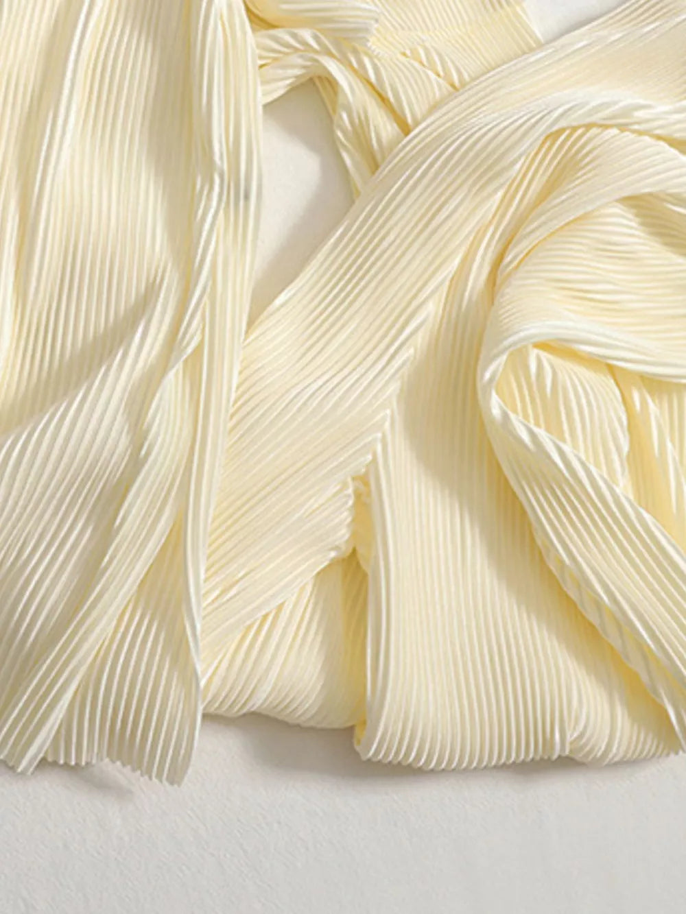 Elegant pleated two-piece set in apricot fabric with flowing texture.