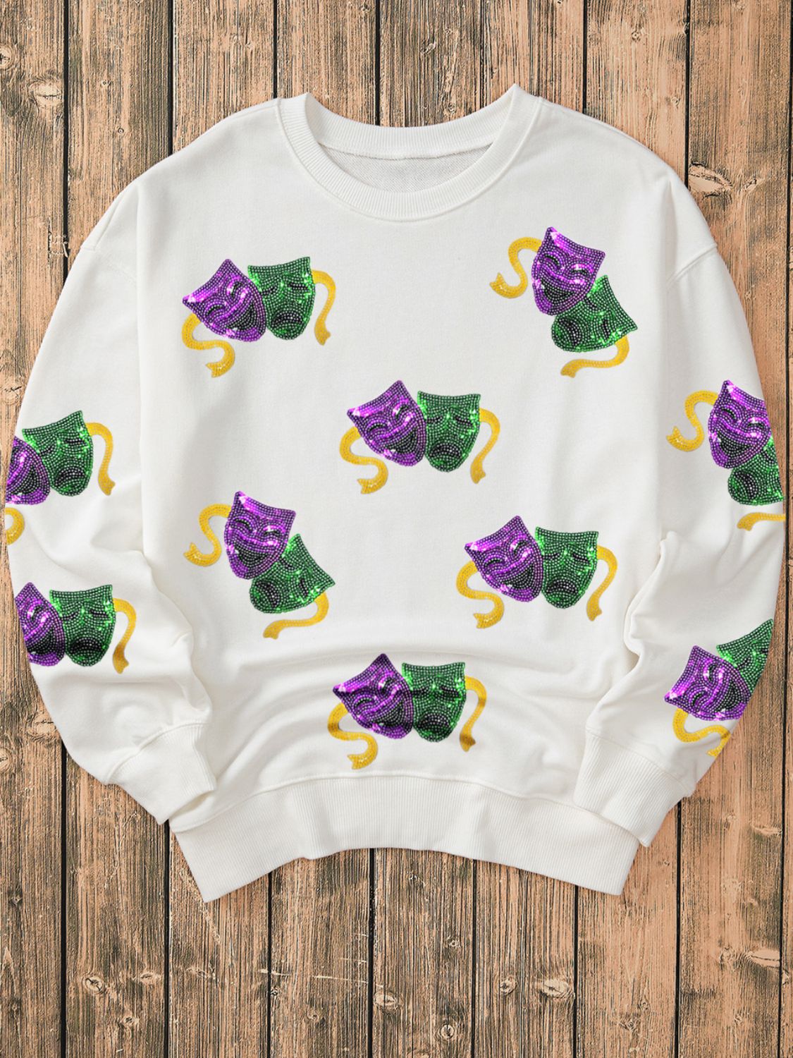 White sweatshirt with sequin Mardi Gras mask motif and gold ribbon detail.