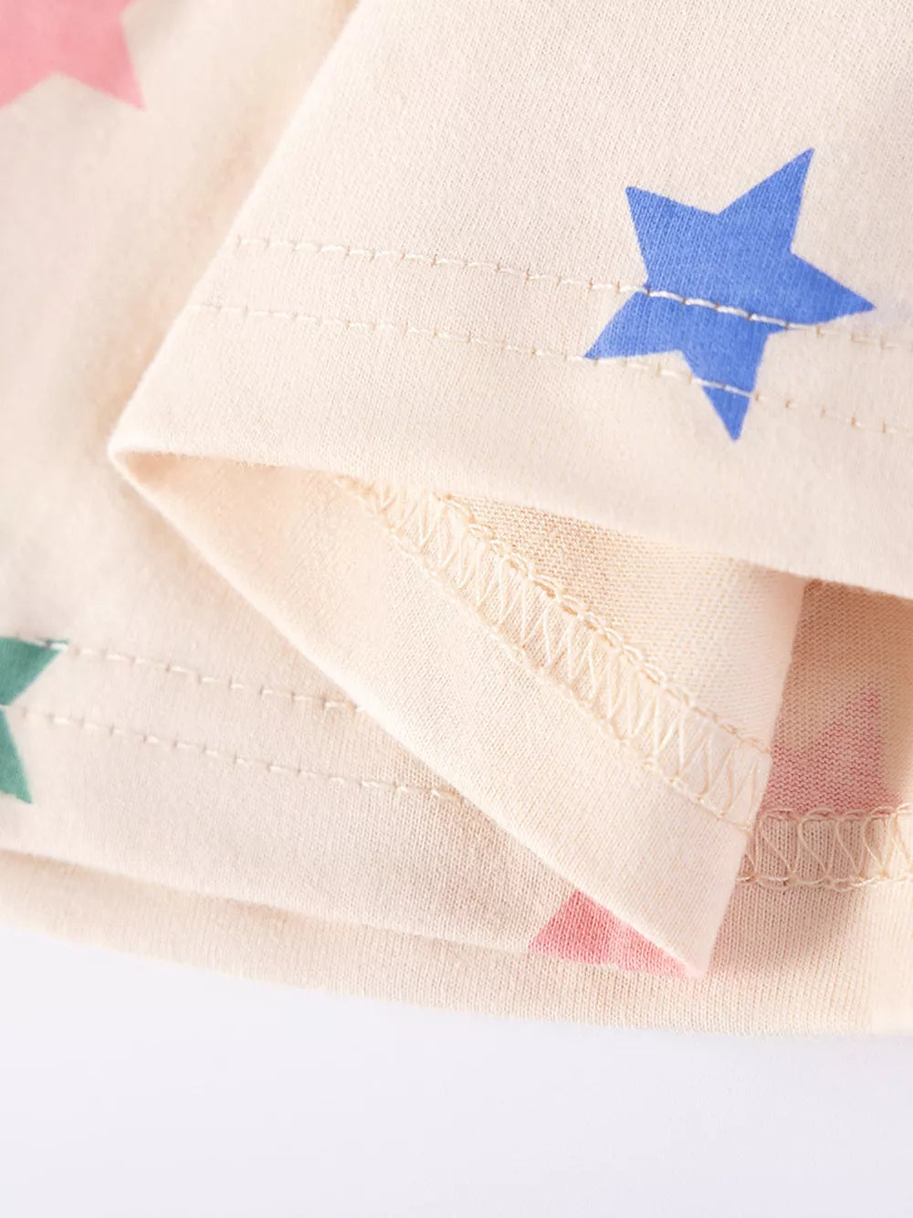 Beige cotton toddler dress with blue, pink, and green star print and ruffled details.