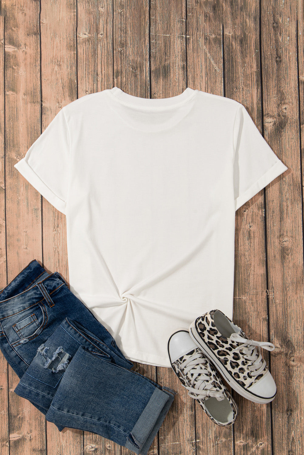 White t-shirt with twisted hem, cuffed sleeves, and crew neck, styled with distressed jeans and leopard print sneakers.