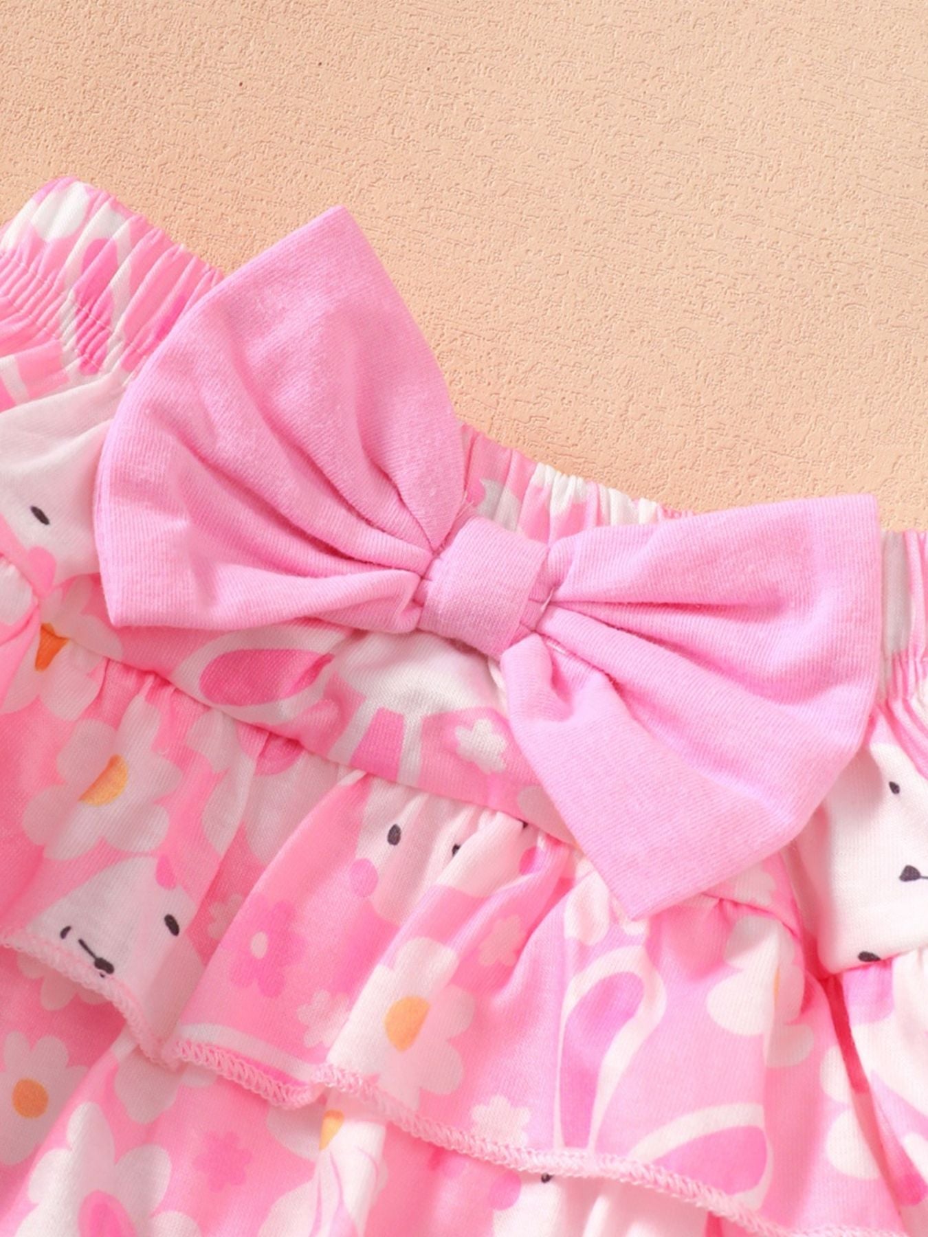 Pink ruffled baby bodysuit and skirt set with floral print and bow detail.