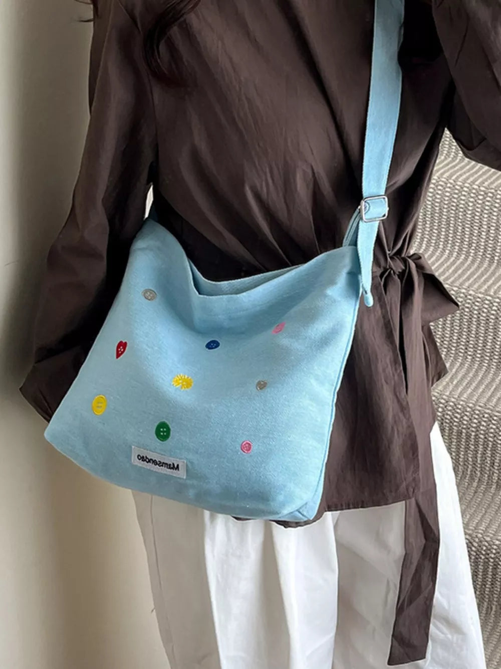 Light blue denim crossbody bag with colorful button embroidery and adjustable strap.