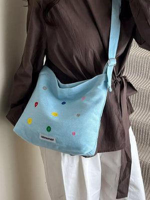 Light blue denim crossbody bag with colorful button embroidery and adjustable strap.