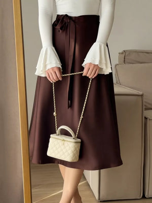 Burgundy satin midi skirt with tie waist and bow detail, worn with a white ruffled sleeve top.