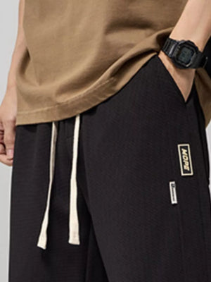 Black relaxed fit drawstring men's joggers with textured fabric and logo patch detail.