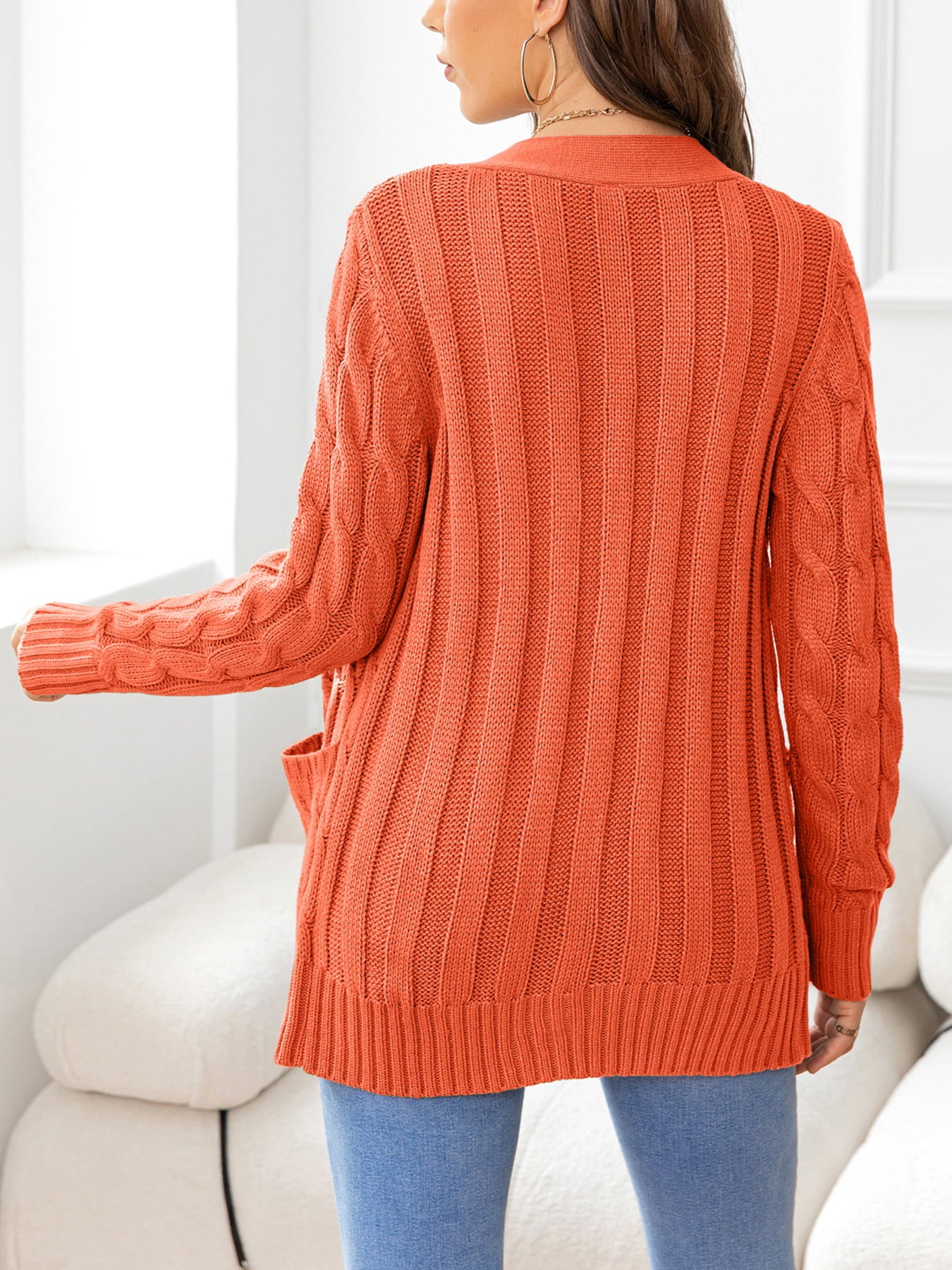 Orange acrylic cable-knit pocket cardigan with ribbed texture and open front.