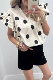 Cream cotton V-neck shirt with black polka dots and ruffled sleeves.