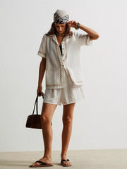 White linen two-piece set with geometric embroidery, button-up shirt, and shorts.