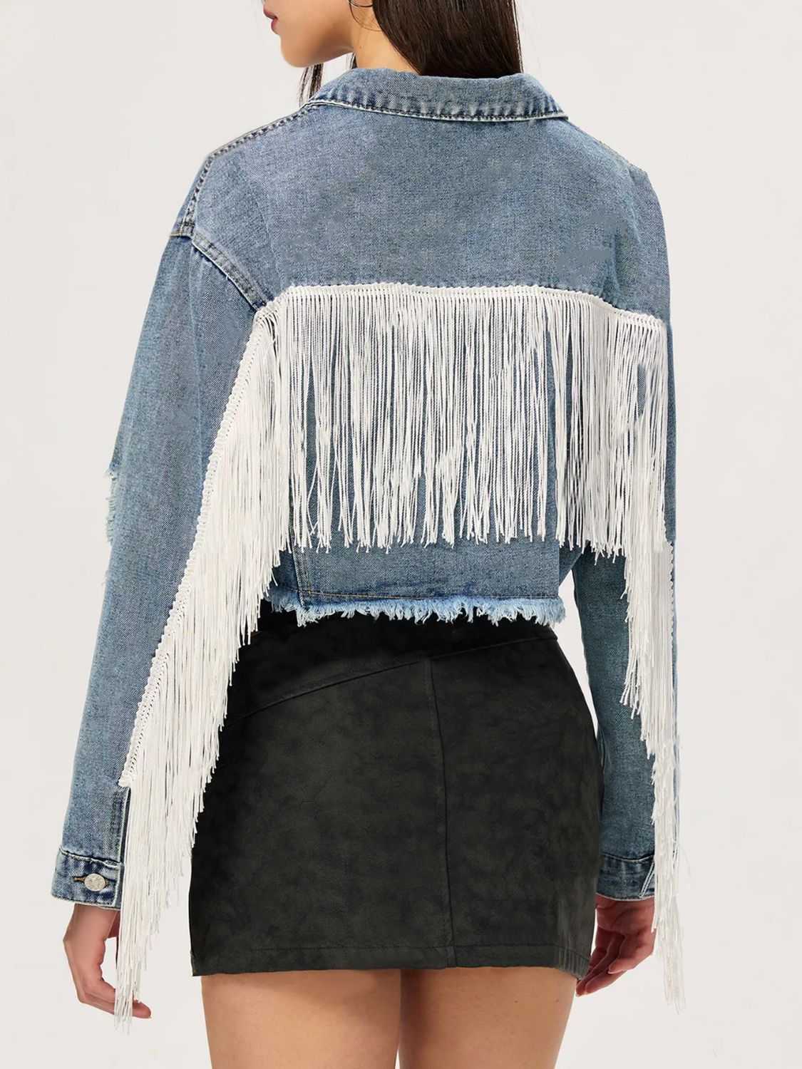 Distressed denim trucker jacket in medium wash with white fringe trim on back and sleeves.