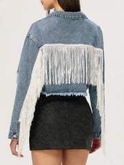 Distressed denim trucker jacket in medium wash with white fringe trim on back and sleeves.