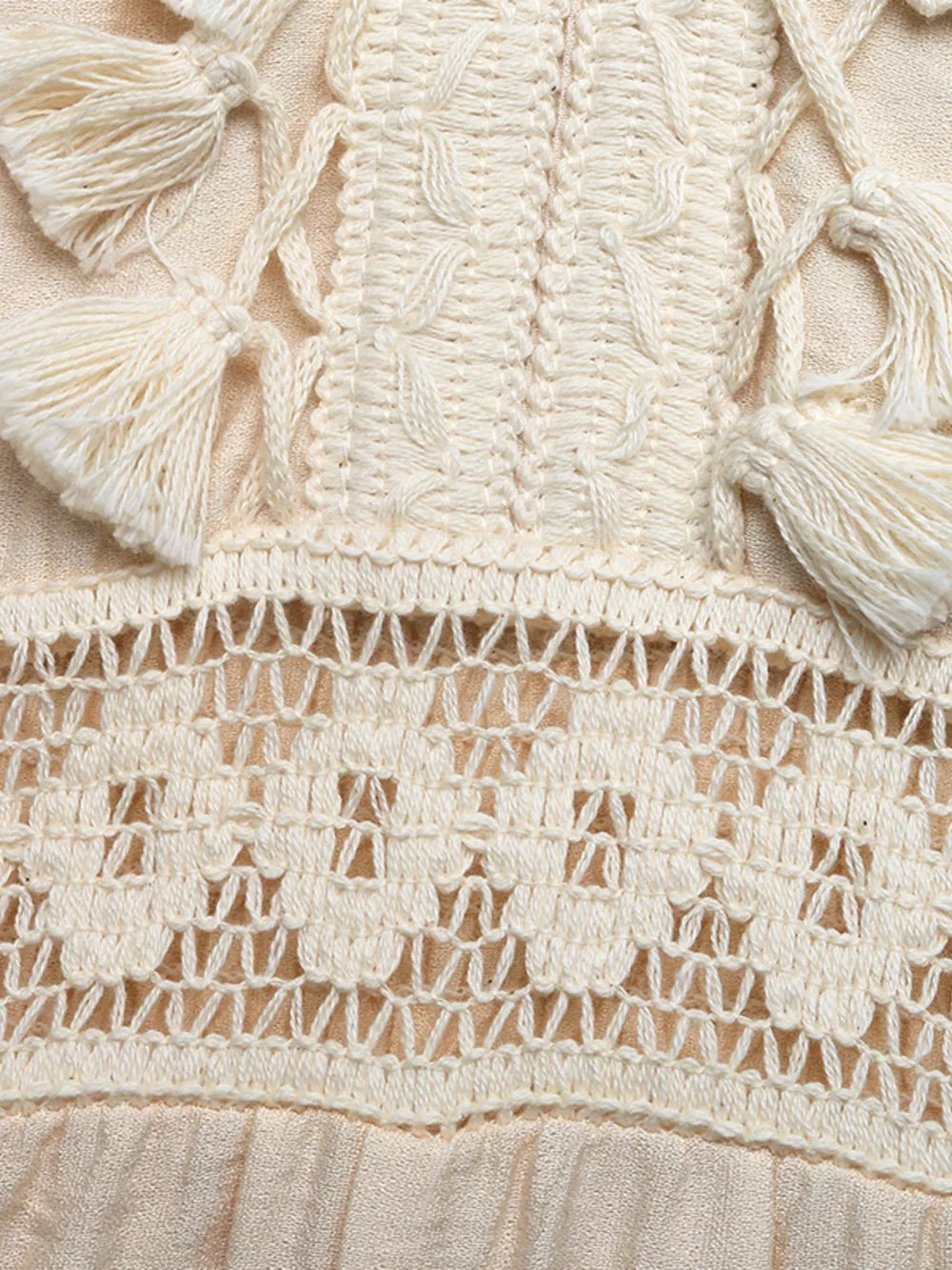 Cream lace-trimmed spaghetti strap romper with crochet detail and tassels.