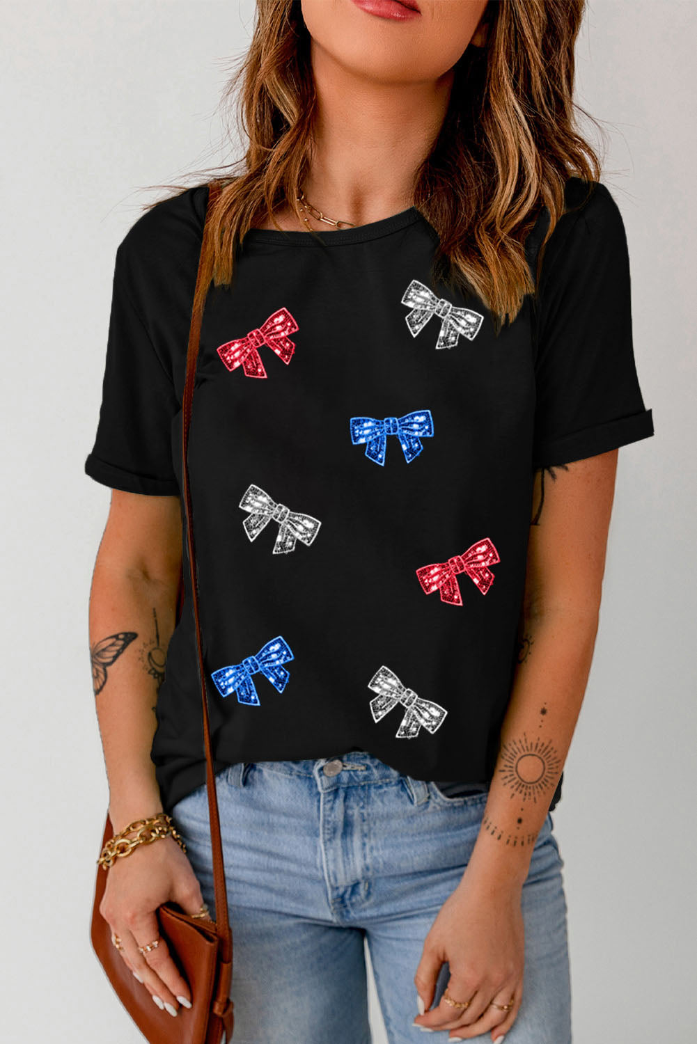 Black crewneck tee with scattered red, blue, and silver bow embellishments.