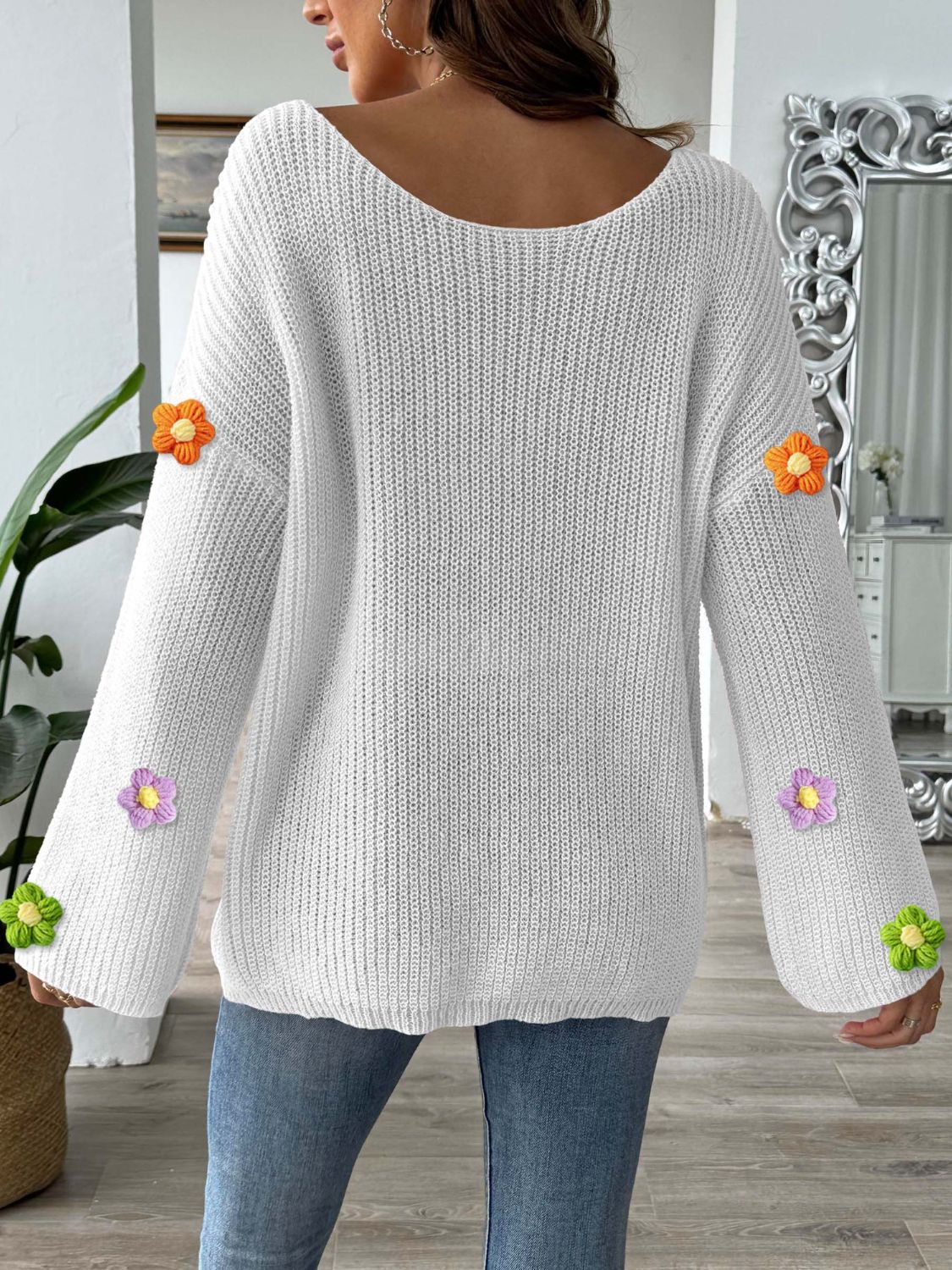 White knit sweater with embroidered floral appliques on sleeves.