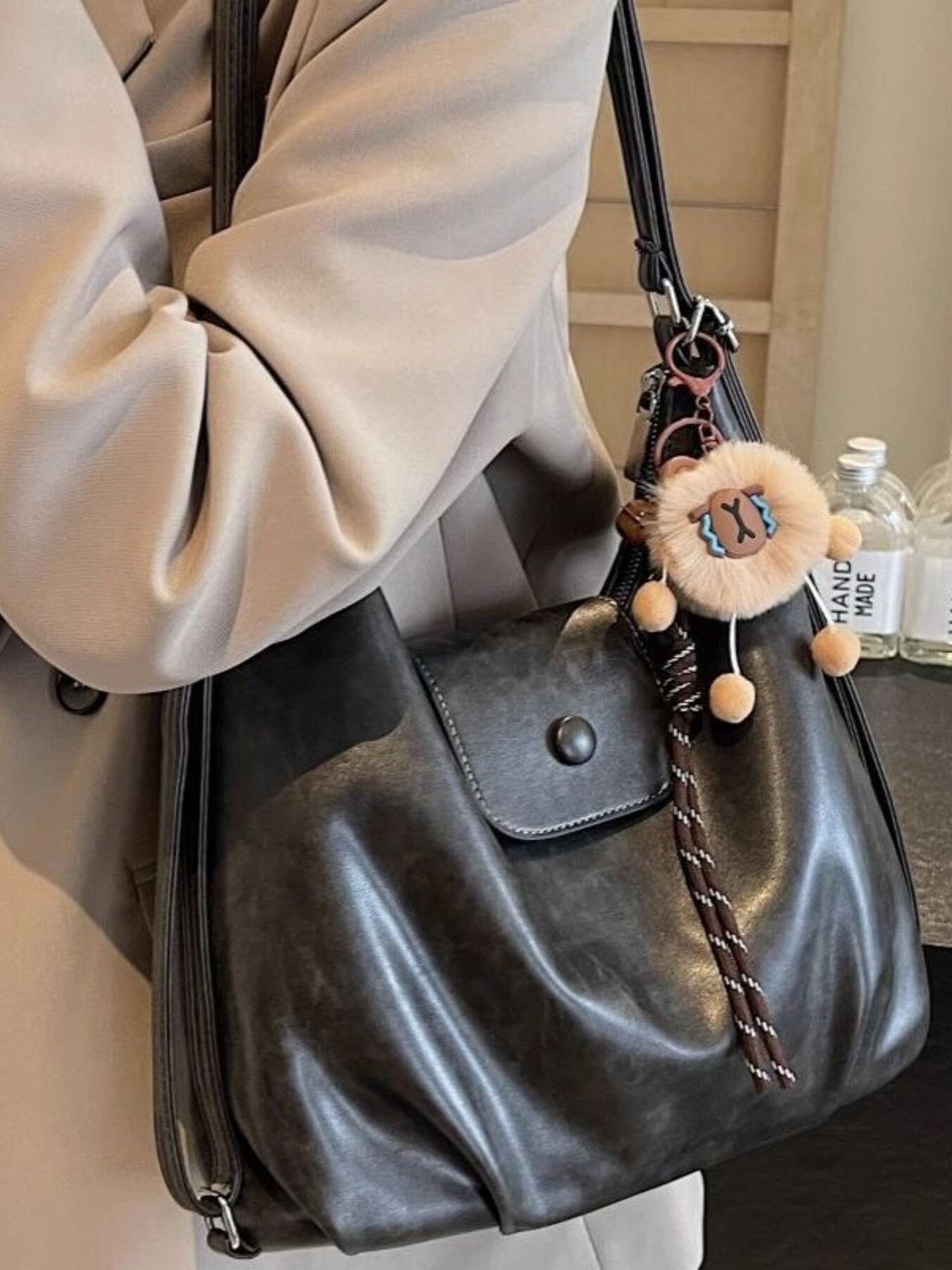 Black slouchy pu leather shoulder bag with braided strap detail and fuzzy charm.