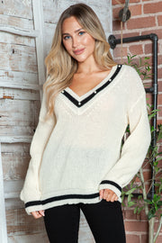 White ribbed knit sweater with V-neck, pearl trim, and black stripes.