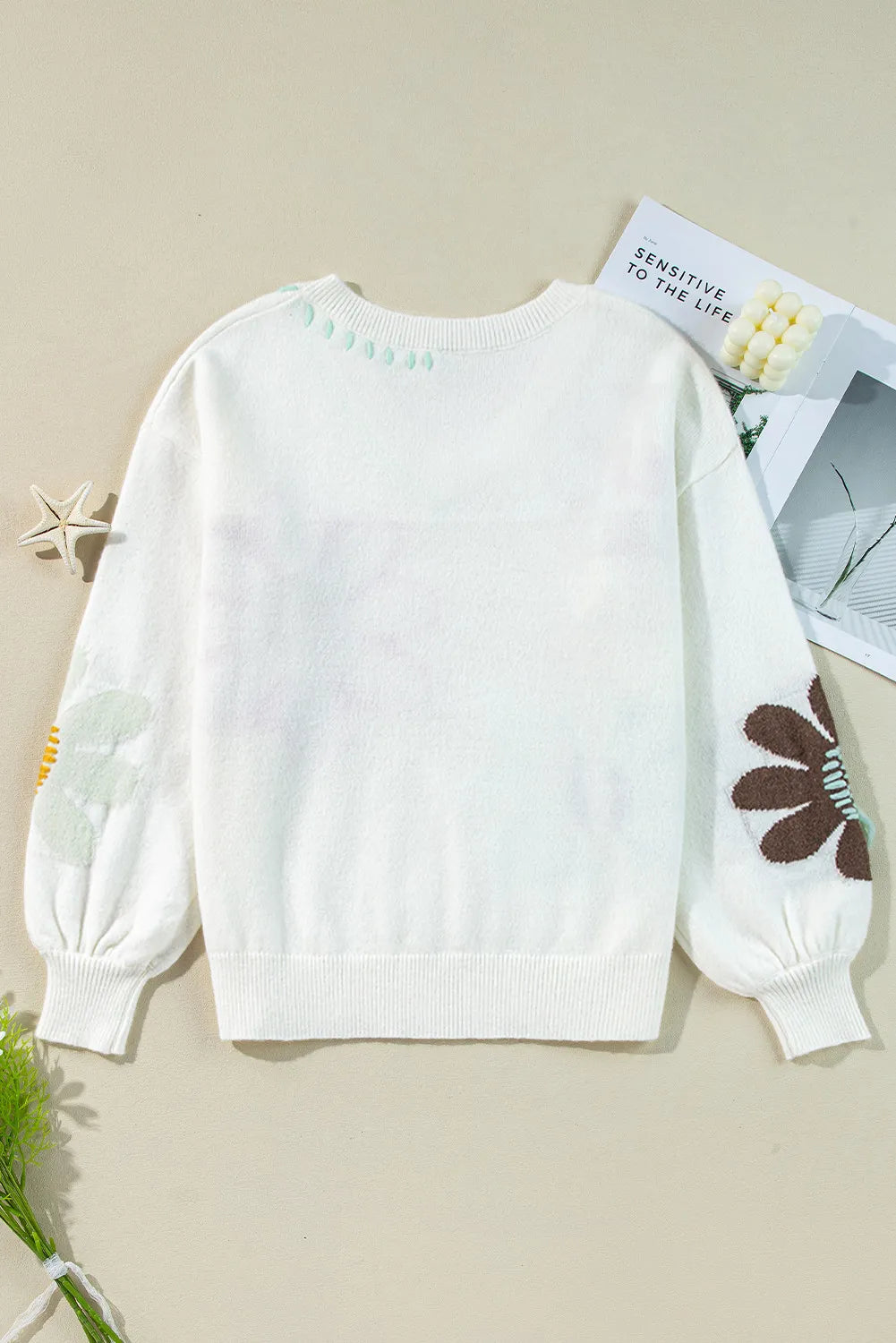 White knit sweater with embroidered floral and leaf details on sleeves and neckline.
