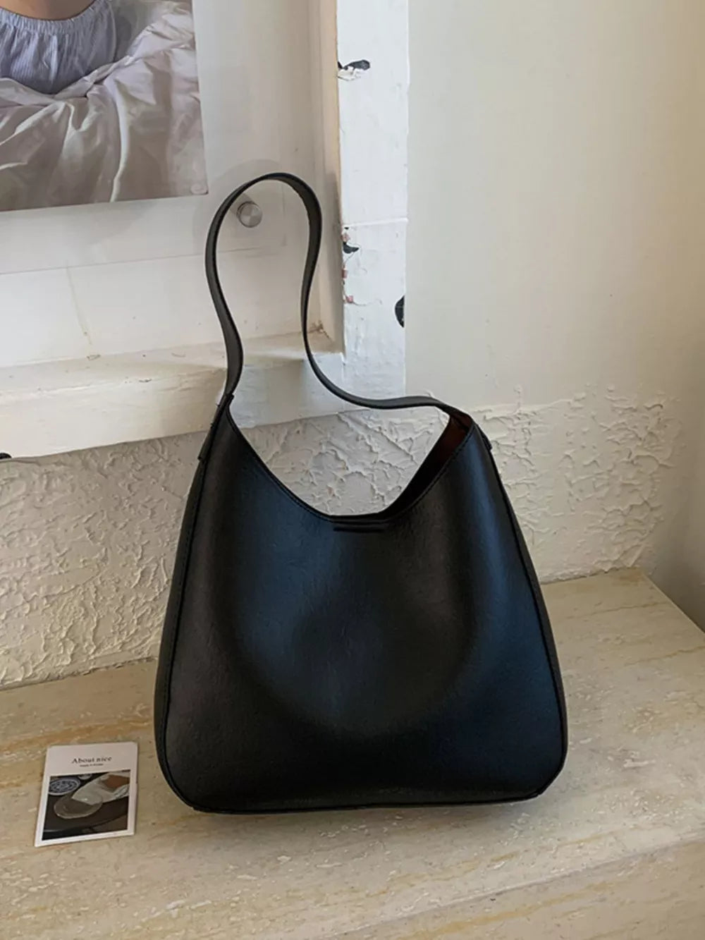 Black pu leather shoulder bag with a sleek, minimalist design and curved strap.