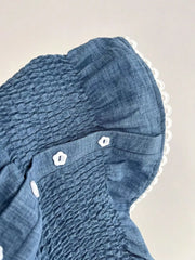 Blue smocked maternity blouse with puff sleeves, decorative buttons, and lace trim.