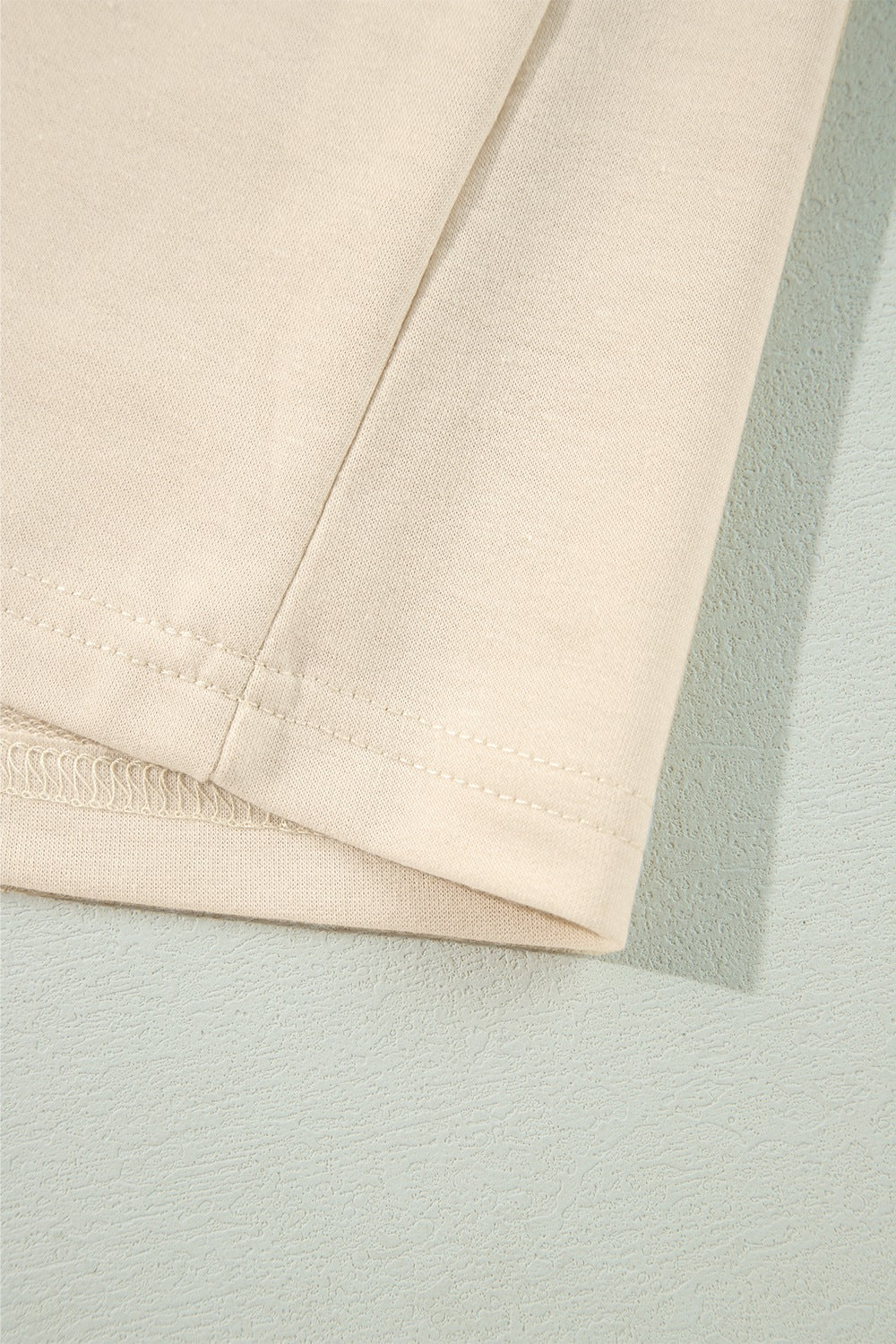 Cream ruffled shoulder sweatshirt detail showing ribbed cuffs and stitching.