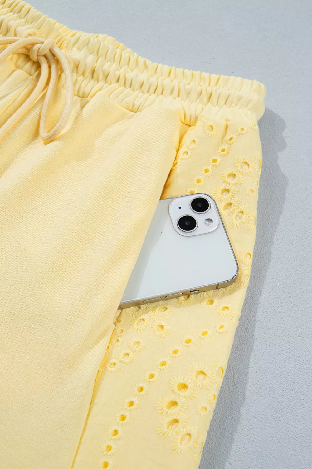 Yellow cotton drawstring pants with eyelet detail and a phone in the pocket.