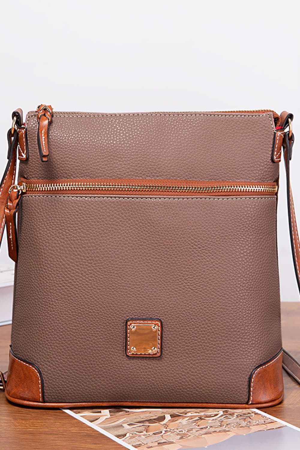 Taupe leather crossbody bag with brown trim and gold hardware.