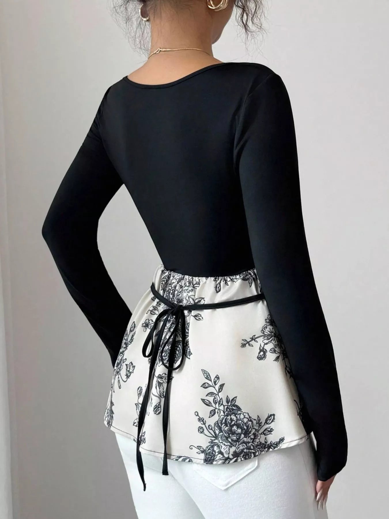 Black long-sleeve top with a peplum hem featuring a black floral print and a tie waist.