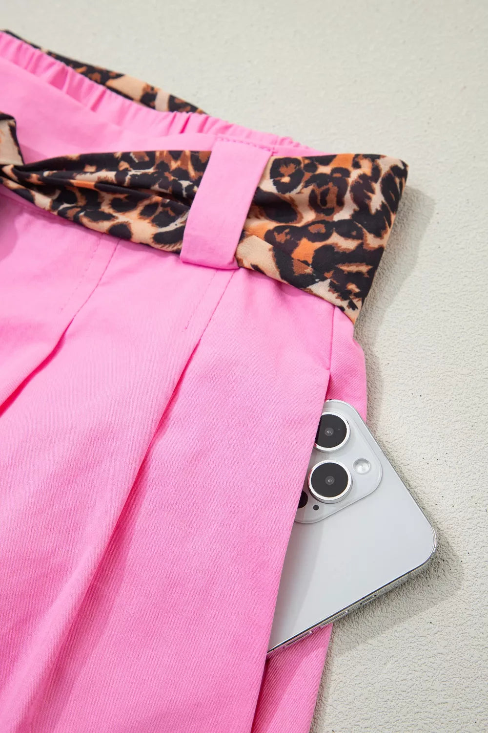 Pink chino shorts with leopard print belt detail and a phone in the pocket.