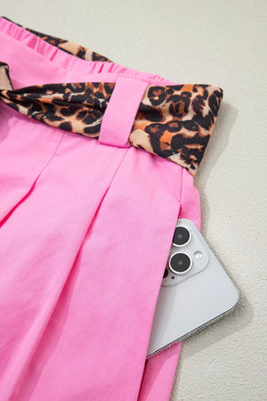 Pink chino shorts with leopard print belt detail and a phone in the pocket.