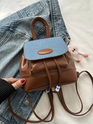 Brown leather mini backpack with blue denim flap and beaded drawstring detail.