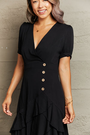 Black viscose wrap dress with button detail, short sleeves, and ruffled asymmetric hemline.