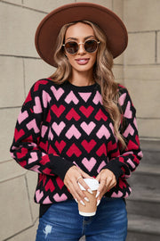 Black knit sweater with allover pink and red heart pattern, crew neck, long sleeves.