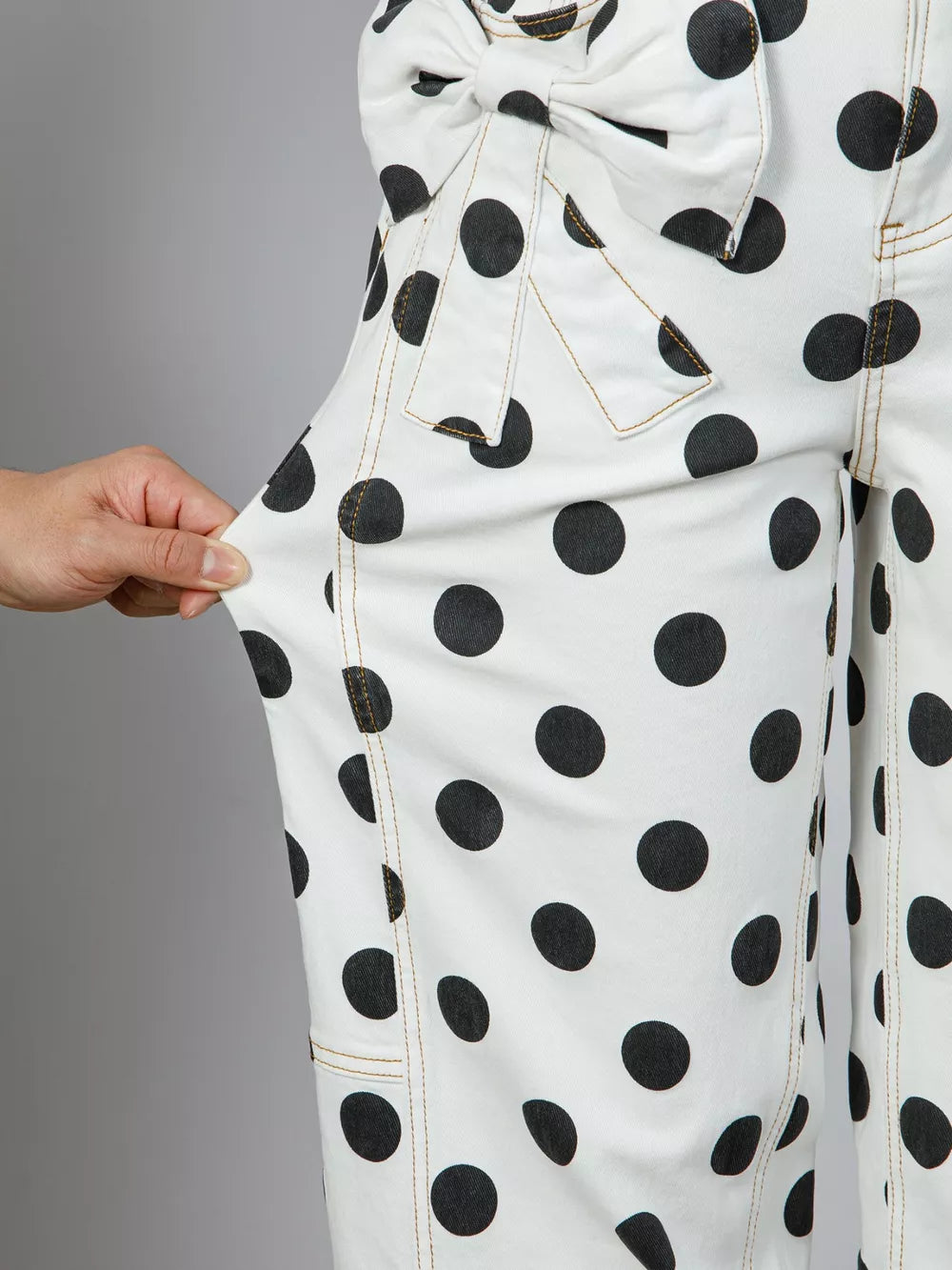 White polka dot high-waisted jeans with bow detail and tan stitching.