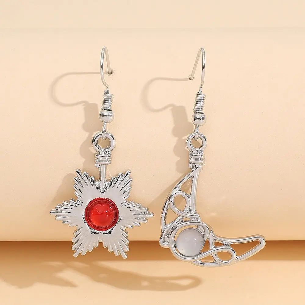 Silver asymmetrical drop earrings with a sun and moon design, featuring a red gem and a white gem.
