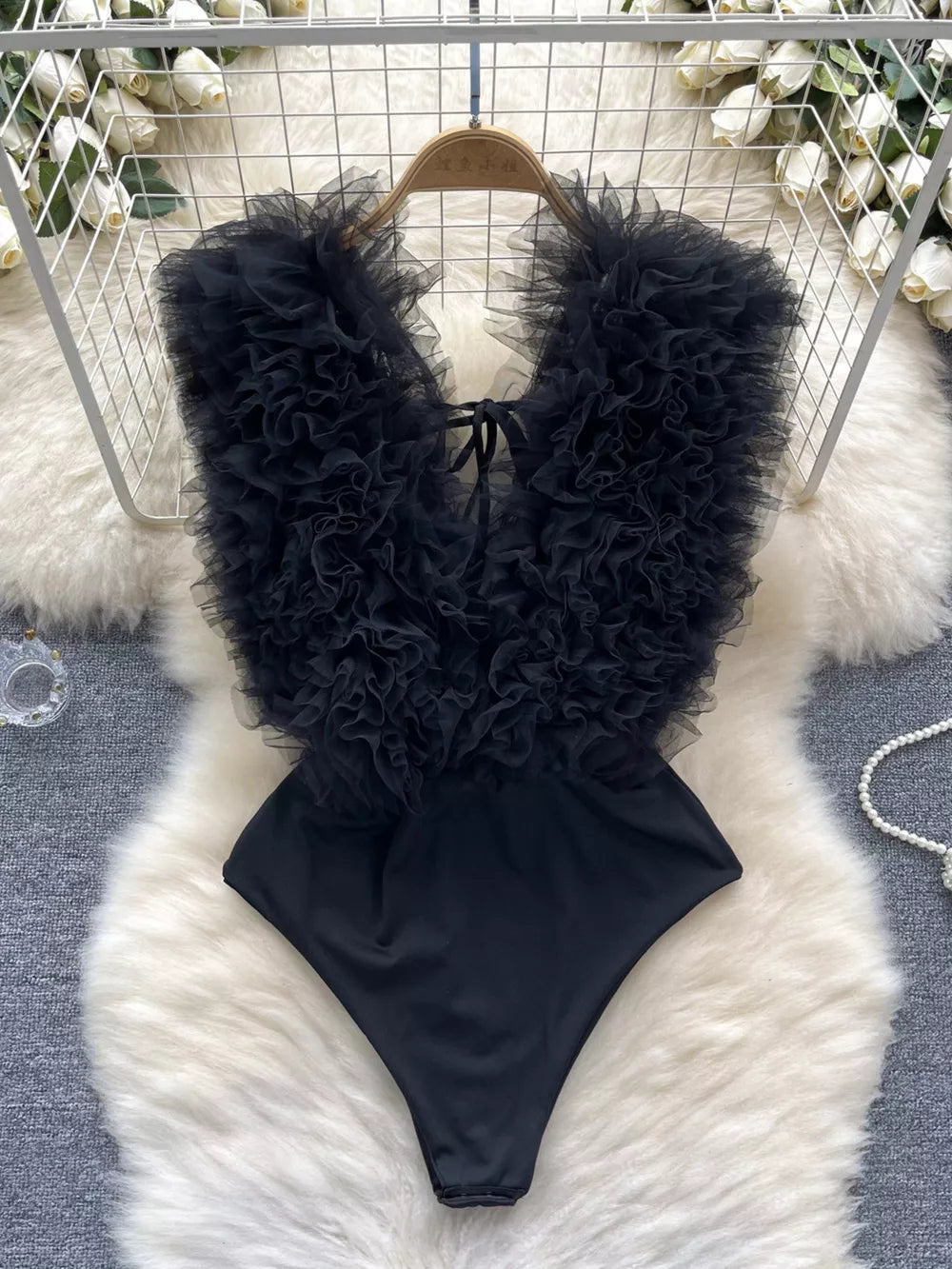 Black ruffled V-neck bodysuit with lace detail and tie closure.