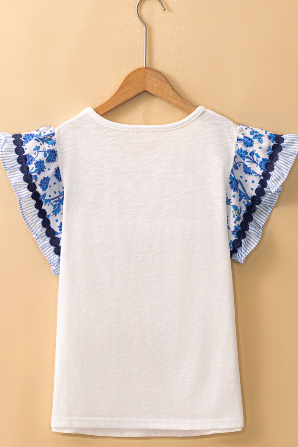 White t-shirt with blue floral embroidered flutter sleeves and striped trim.