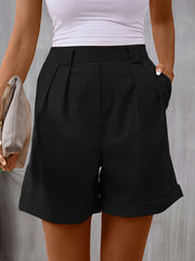 Black pleated tailored bermuda shorts with cuffed hems and a cinched waist.