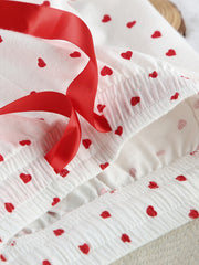 White cotton pajama set with red heart pattern and red ribbon detail.