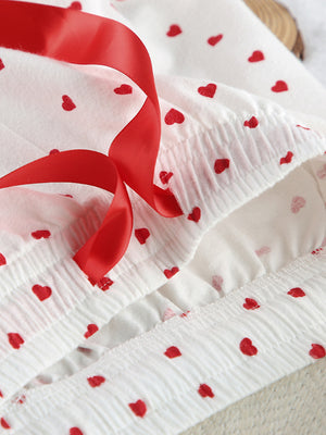 White cotton pajama set with red heart pattern and red ribbon detail.
