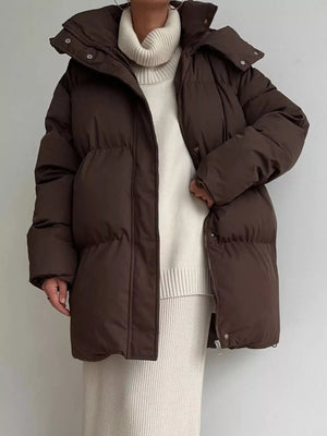 Dark brown puffer trench coat with hood and buttoned closure, worn over a cream turtleneck sweater.