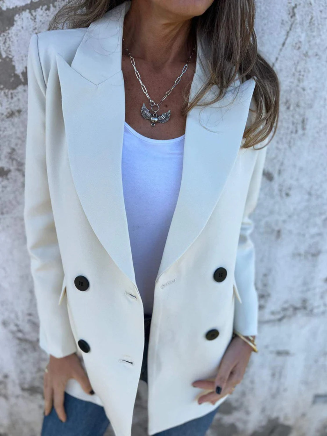 Ivory double-breasted blazer with sculpted lapels and black buttons, styled with a white tank and necklace.