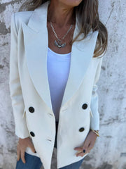 Ivory double-breasted blazer with sculpted lapels and black buttons, styled with a white tank and necklace.