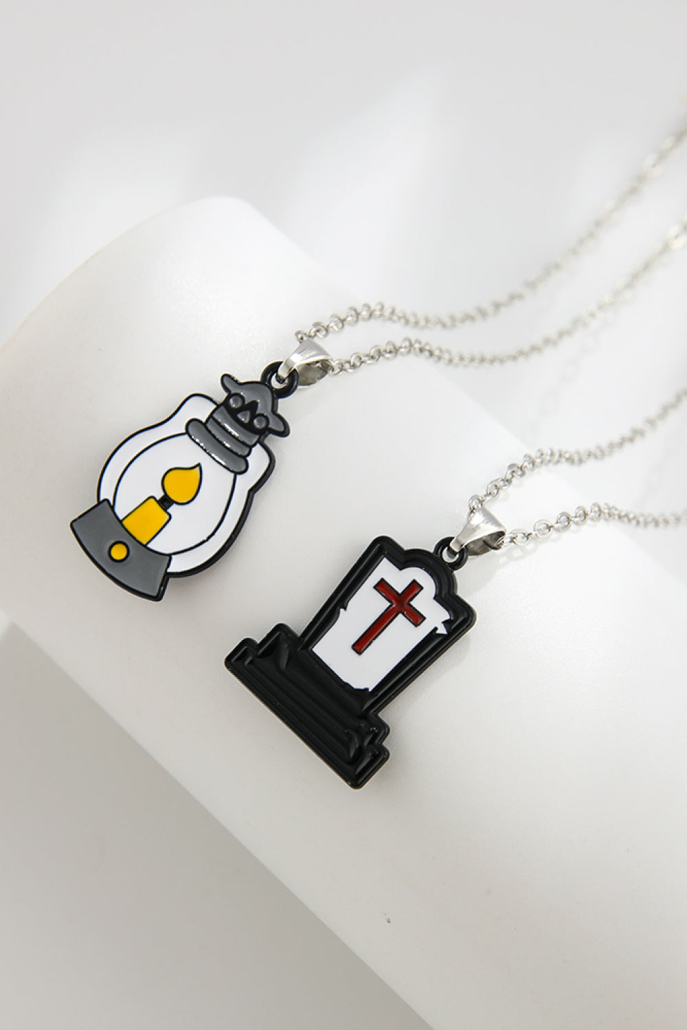 Spooky Season enamel pendant necklaces, one a lantern with yellow flame, one a tombstone with red cross.