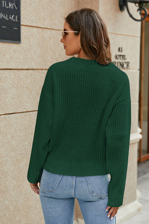 Green ribbed knit sweater with a cross-front detail and crew neck, styled with jeans.