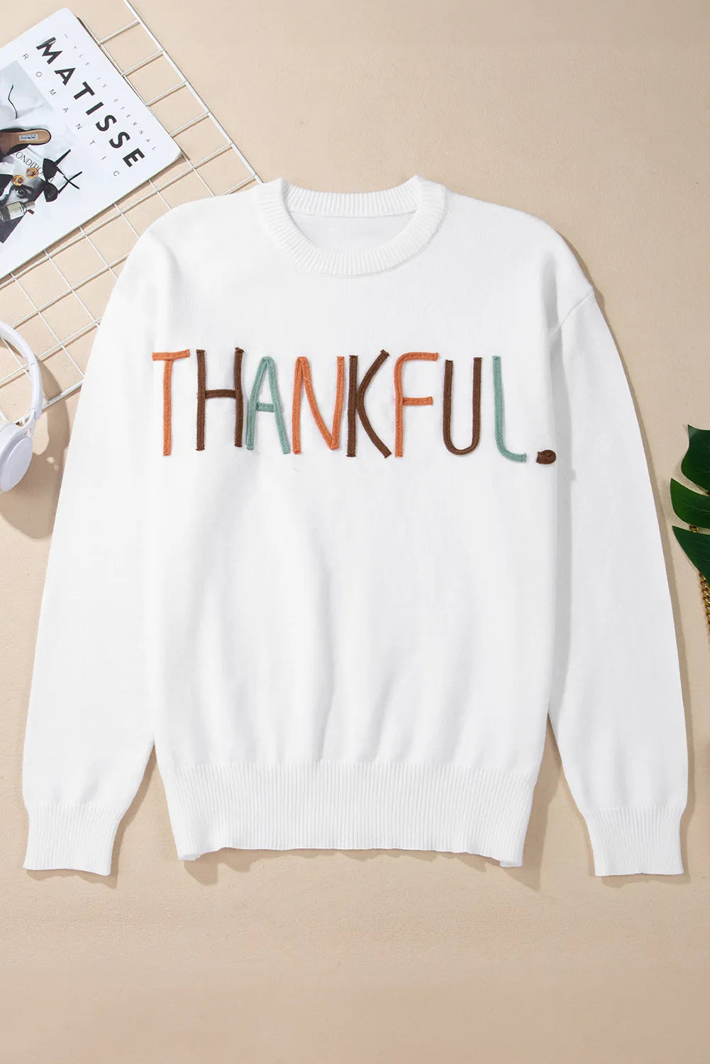White crewneck sweater with embroidered "THANKFUL" text in multi-color yarn.