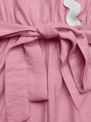Pink maternity wrap romper with tie waist and white scalloped trim detail.