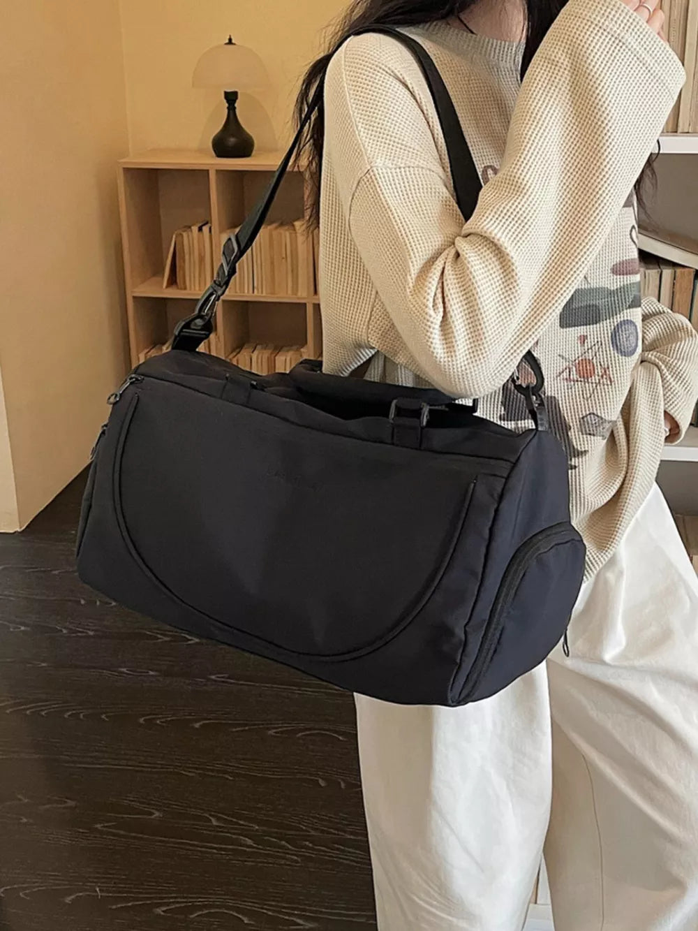 Black medium duffle bag with adjustable strap and side pocket, worn crossbody.