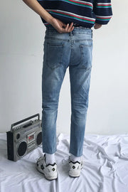 Medium wash denim jeans with raw hem and slim fit, styled with sneakers.