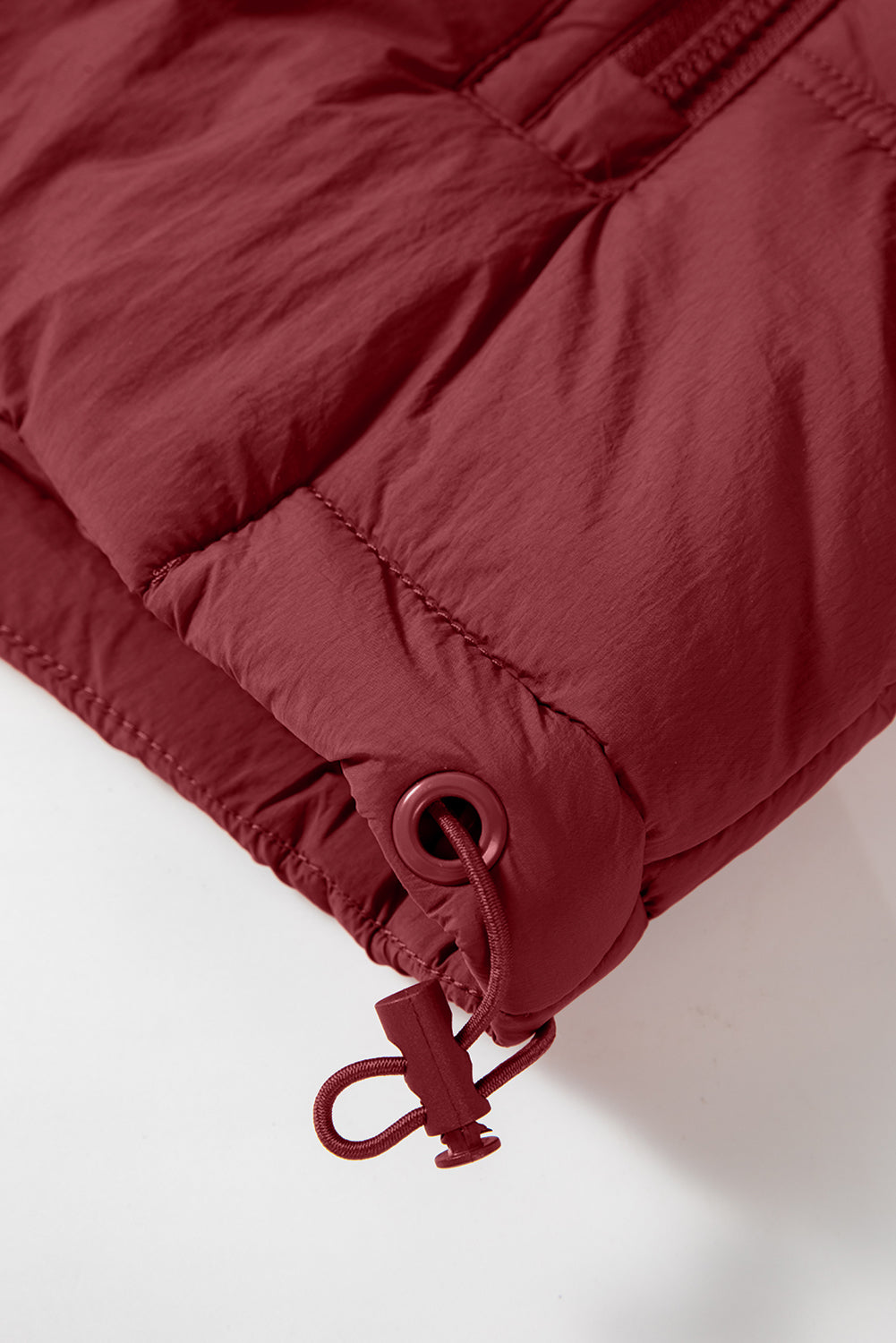Burgundy quilted puffer vest detail showing adjustable drawcord hem with toggle.