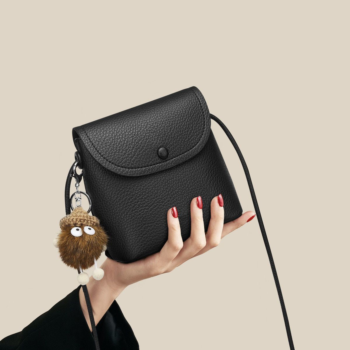 Black pebbled pu leather crossbody bag with button closure and fuzzy charm.
