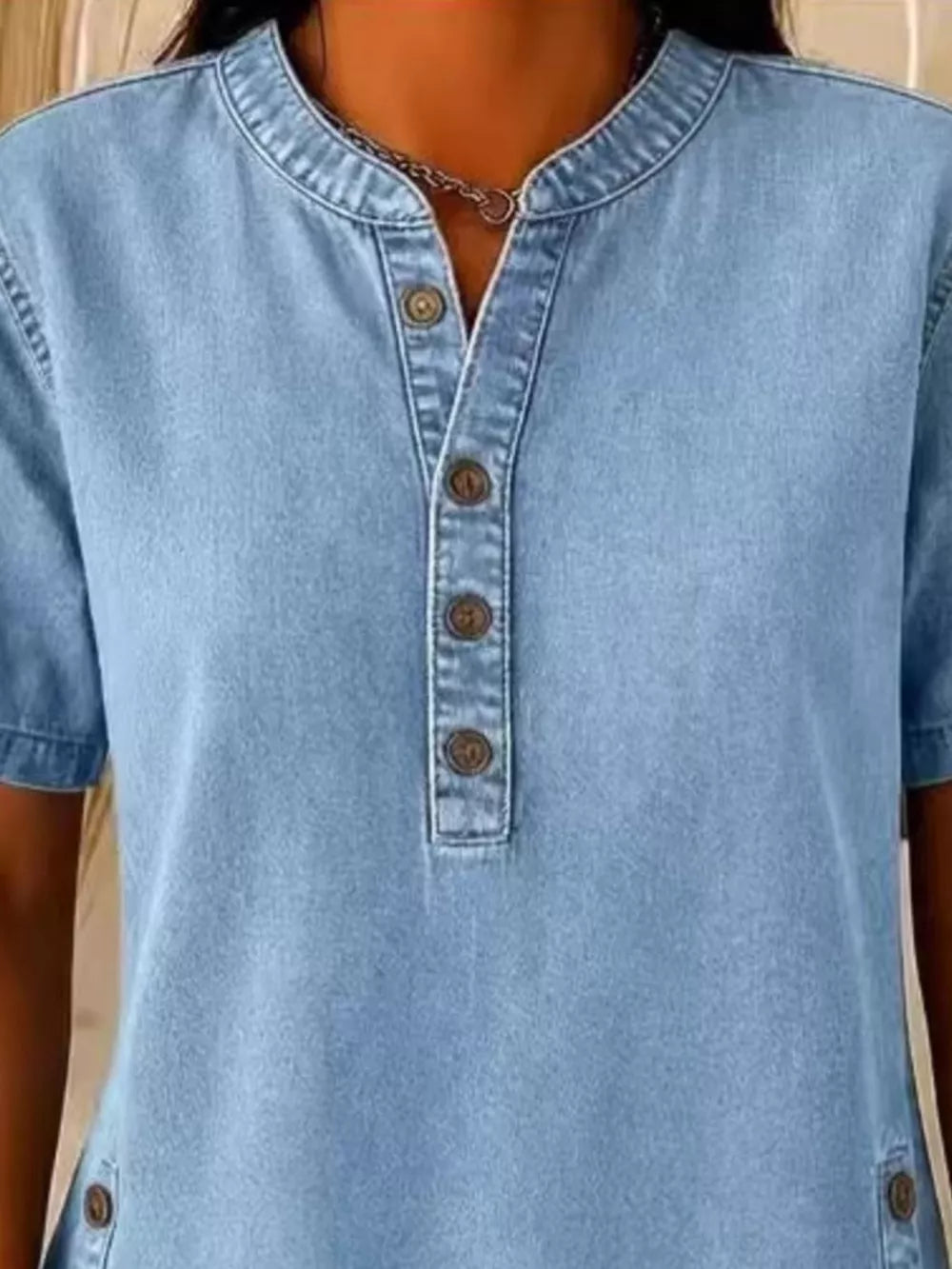 Light blue denim-inspired short sleeve button blouse with band collar and button detail.